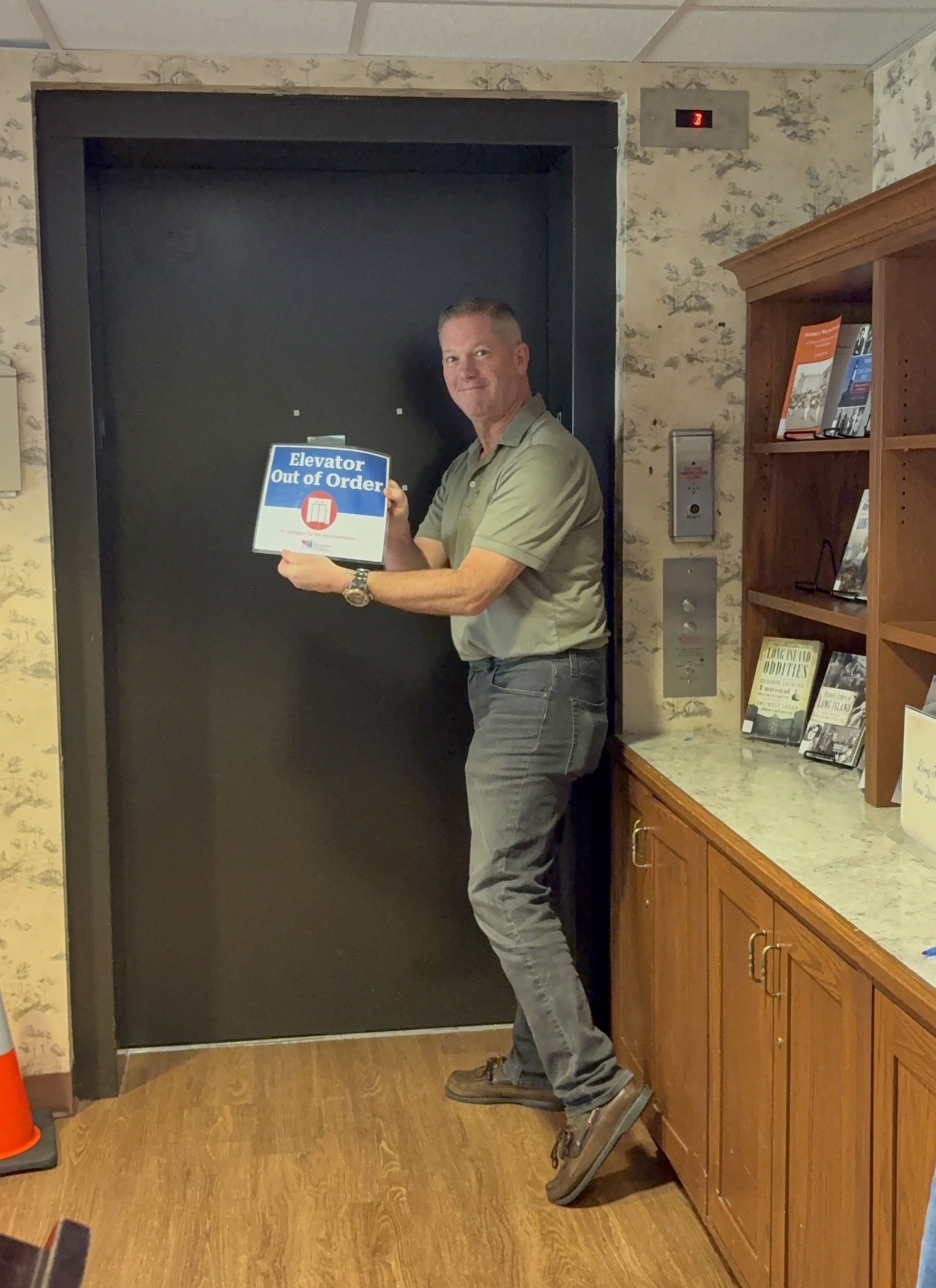 gentleman with dark pants and green shirt removing a sign from the elevator
